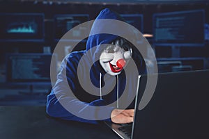 Hacker wearing clown mask hacking on a laptop computer