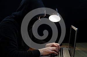 Hacker wearing hoodie and balaclava sitting typing on laptop keyboard