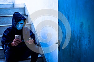 Hacker wearing a white mask and hoodie holding credit card and using smartphone. Cyber crime concept, Data thief, internet attack