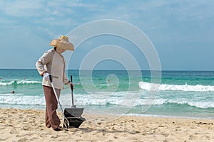 Hainan Island, Sanya, China - May 16, 2019: A cleaning lady picks up trash on Hainan Beach with special handy forceps