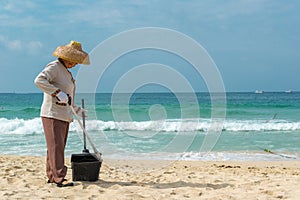 Hainan Island, Sanya, China - May 16, 2019: A cleaning lady picks up trash on Hainan Beach with special handy forceps