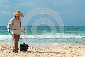 Hainan Island, Sanya, China - May 16, 2019: A cleaning lady picks up trash on Hainan Beach with special handy forceps