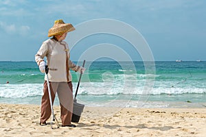 Hainan Island, Sanya, China - May 16, 2019: A cleaning lady picks up trash on Hainan Beach with special handy forceps