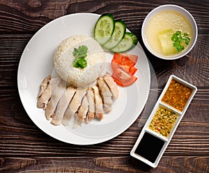 Hainanese chicken rice with soup and three sauces on dark wood table texture