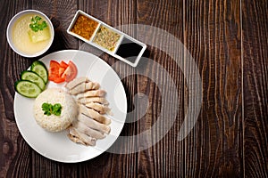 Hainanese chicken rice with soup and three sauces on dark wood table texture with copy space