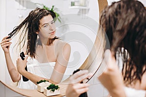 Hair and body care. Young happy woman in white towel applying conditioner mask on hair in bathroom, mirror reflection. Slim