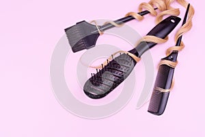 Hair brush, comb and brush for coloring hair among blond curls on a pink background