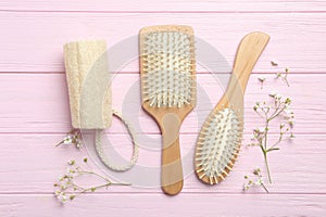 Hair brushes, bast wisp and small flowers on pink wooden background, flat lay photo