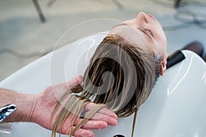 Hair care in modern spa salon. Male hairdresser washing teen girl's hairs