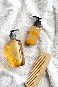 Hair care products design. Yellow dispenser bottles with shampoo and lotion, wooden hair comb on white towel in bathroom.