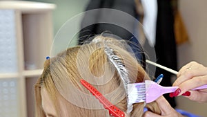 Hair coloring. Close-up of a stylist\'s hands using a professional comb and coloring the roots of a client\'s hair.