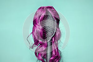 Hair coloring. Comb with pink wig on turquoise background, similar to woman's head. Concept of hair care, baldness