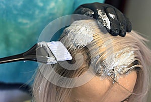 Hair coloring Hairdresser in gloves with a brush paints the roots of hair to a girl with a light color