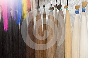Hair of different colors for extension hang on a stand in a beauty salon. Hair beauty and health concept