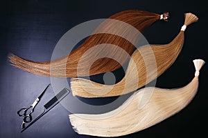 Hair extensions of three colors on a dark background with Scissors and comb. copyspace top view.