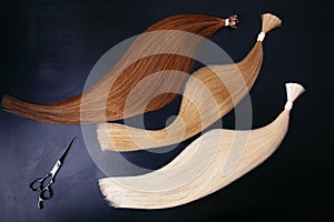 Hair extensions of three colors on a dark background with scissors. copyspace. top view. photo