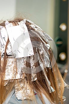 Hair foiled during hair dyeing of a young woman in hair salon close up.