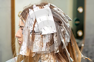 Hair foiled during hair dyeing of a young woman in hair salon close up.