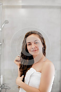 Hair. Girl touching her hair and smiling while looking in the mirror.Portrait of happy young woman with wet hair in bathroom.