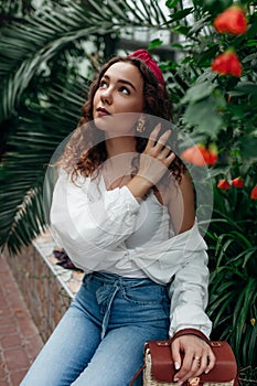 Hair hoop and purse. Young fashionable woman wearing stylish female accessories in garden among flowers.