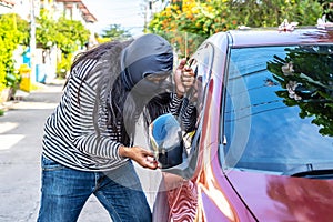 Hair long Male thief wearing black robbery mask trying to open car window with ruler, Car thief concept