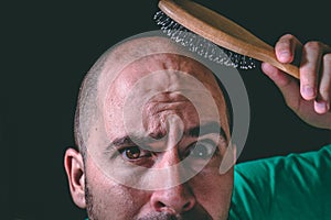Hair loss concept. Bald man using hair brush on non existent hair.