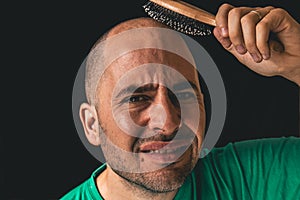 Hair loss concept. Bald man using hair brush on non existent hair.