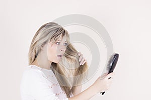 Hair loss. Depressed young woman looking at her hairbrush and expressing negativity