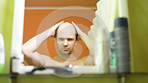 Hair loss problem. balding young man looks in the bathroom mirror