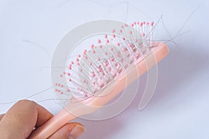 Hair loss problems with hand holding a pink hairbrush on white background. Falling black hair clinging to the comb