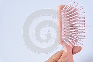 Hair loss problems with hand holding a pink hairbrush on white background. Falling black hair clinging to the comb