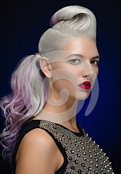 Hair and make-up theme: beautiful young blond woman with creative hair styling with red lips on a dark blue background in studio