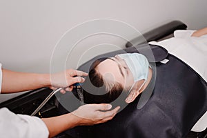 Hair salon concept a male hairdresser holding a water shower gently washing a female customerâ€™s hair