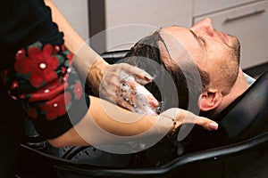 Hair salon master washing client hair at barber shop. Male client getting haircut by hairdresser. Hair care, beauty