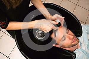 Hair salon master washing client hair at barber shop. Male client getting haircut by hairdresser. Hair care, beauty