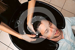 Hair salon master washing client hair at barber shop. Male client getting haircut by hairdresser. Hair care, beauty