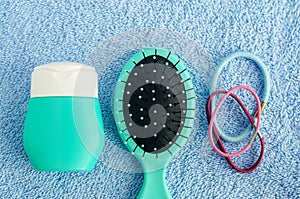 Hair shampoo mask, conditioner, face cream, sunscreen lotion, hair brush and three scrunchies on the blue towel. Top view