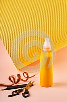 Hair spray bottle with curly lock of hair, scissors and a comb on beige and yellow background.