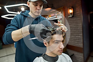 Hair styling. Close up shot of professional male barber making haircut for his client, working with scissors and hair