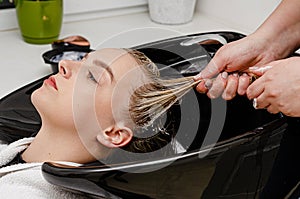 Hair stylist applying hair mask treatment on wet hair in a washing sink