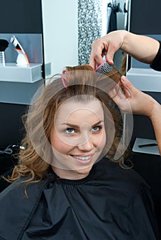 Hair stylist curling woman hair in salon