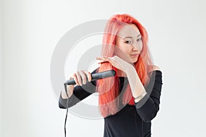 Hair Stylist, hairdresser and people concept - young woman with colored hair holding curling iron over white background