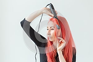 Hair Stylist, hairdresser and people concept - young woman with colored hair holding curling iron over white background