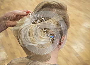 Hair stylist makes the bride a wedding hairstyle with hair detail accessory, closeup rear view.