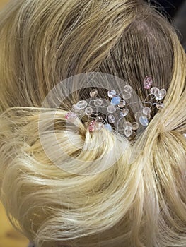 Hair stylist makes the bride a wedding hairstyle with hair detail accessory, closeup rear view.