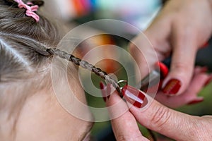 Hair stylist makes a hairstyle, attaches an accessory decor ring to the braid