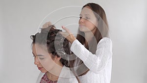 A hair stylist makes a hairstyle for a young beautiful girl with long dark hair