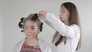 A hair stylist makes a hairstyle for a young beautiful girl with long dark hair