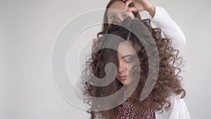 A hair stylist makes a hairstyle for a young beautiful girl with long dark hair