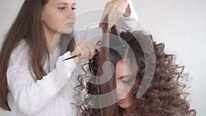 A hair stylist makes a hairstyle for a young beautiful girl with long dark hair